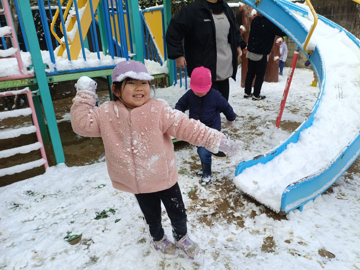 雪が積もった園庭で雪玉を持って笑う子ども